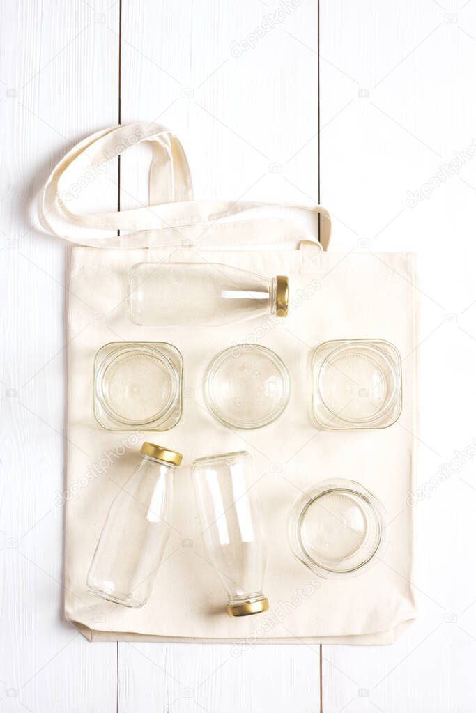 Waste-free shopping set. A reusable woven bag rests on a white surface with glass bottles and jars on top. Eco-friendly lifestyle. Vertical orientation, knolling.