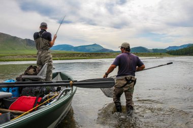 Moğolistan, Moron, Moğolistan 'daki Delger Moron nehrinde, bir tekneden gelen Taimen alabalığıyla uçan bir balıkçı - 14 Temmuz 2014