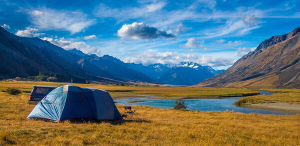 A tent pitched beside the Ahuriri River, surrounded by mountains, in Cantebury, South Island, New Zealand