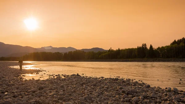Gün batımında Skeena Nehri 'nin kıyısındaki çakıl barında yürüyen bir balıkçı, Ferry Adası, Terrace, British Columbia, Kanada