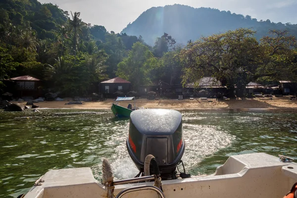 The stern and outboard motor of a boat leaving a tropical island in morning, Tiomen Island, Malaysia