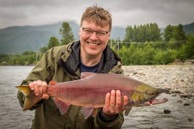A happy fisherman holding up a red sockeye salmon, caught on the kitimat river, British Columbia, Canada clipart