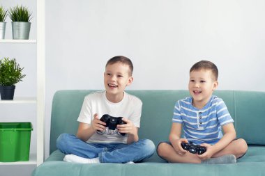 Küçük çocuklar mavi bir kanepede video oyunu oynuyorlar.