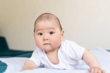 Yeni doğmuş beyaz elbiseli yakışıklı Asyalı bir çocuk karnının üzerine yatar ve çerçevenin içine bakar..