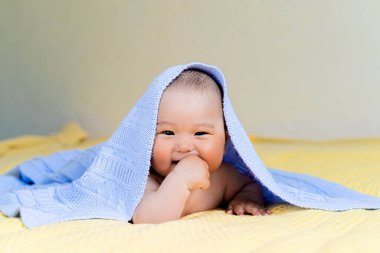 Yeni doğmuş Asyalı bir bebek battaniyenin altında yatıyor ve gülüyor..