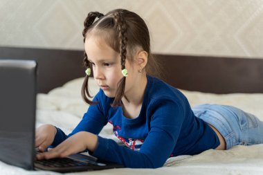 Kız laptopun yanındaki yatakta oturuyor ve kafasını çeviriyor.