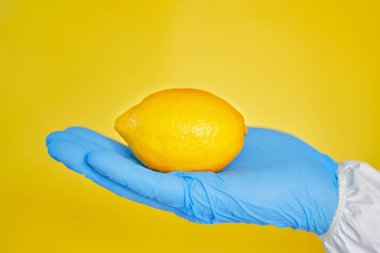 Sarı arka planda eldivenli sarı limon. Lemon virüsler için iyi bir ilaçtır..