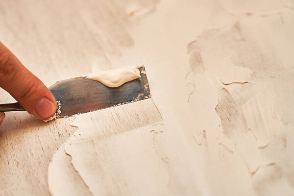 a small spatula applies putty to the wooden surface to create a structural background