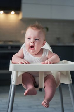 Beyaz elbiseli küçük bir çocuk yüksek sandalyede oturup esniyor..