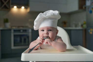 Beyaz elbiseli küçük bir çocuk yüksek bir sandalyede oturur ve gülümser..