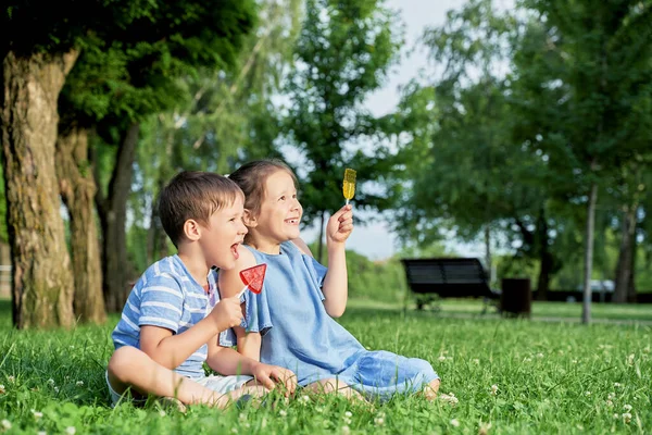 两个有棒棒糖的孩子坐在绿草上 — 图库照片