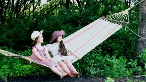 Kleine meisjes in de zomer met hoeden zitten op een hangmat en lachen — Stockvideo