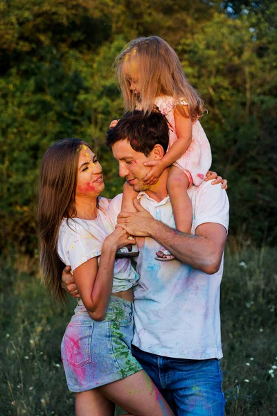 beautiful family, mom, dad and daughter play with Holly colors. multi-colored paint on clothes and face.