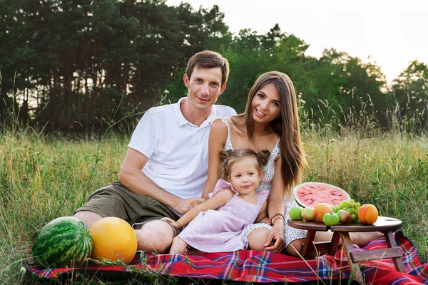 beautiful family, mom, dad and daughter sitting on a picnic with watermelon.