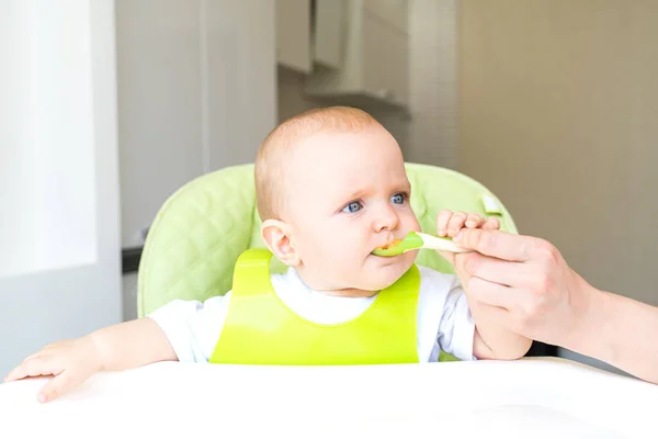 一个长着蓝眼睛和金发的小孩坐在高椅上 吃着第一个饵 健康饮食 6个月大 — 图库照片