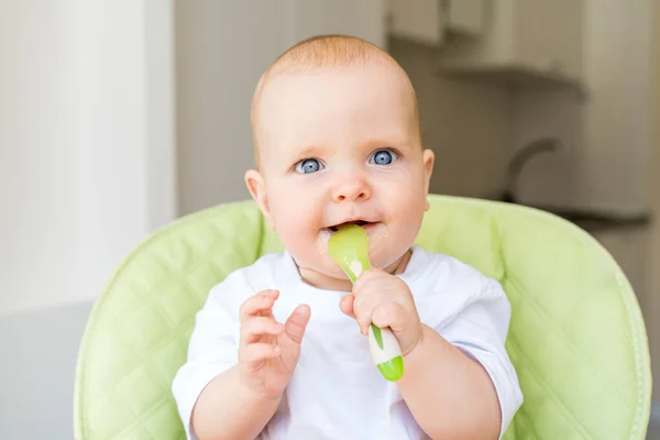 一个长着蓝眼睛和金发的小孩坐在高椅上 吃着第一个饵 健康饮食 6个月大 — 图库照片