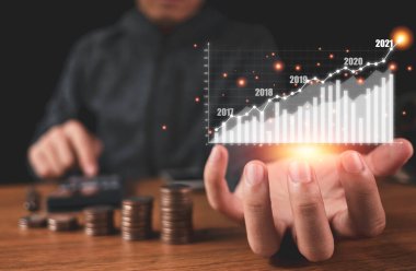 Sanal grafik ve yazılar elinde tutan bir işadamı. Para yığını olan bir deftere kar veya kâr sağlıyor. İş yatırımı ve tasarruf kar kavramı.