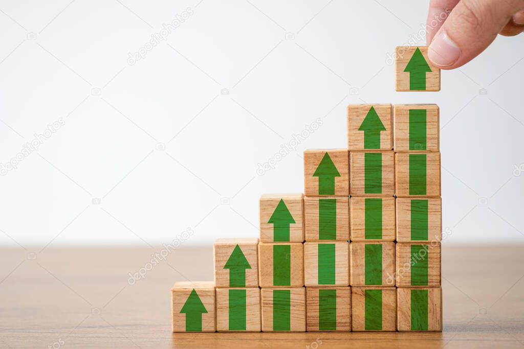 Hand putting wooden cubes block which print screen increase or up green arrow. It is symbol of economic investment profit growth.