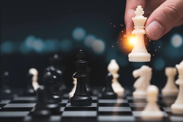 Businessman hand holding and moving white king chess figure with competitor to success play. Business management   competition and leadership concept.