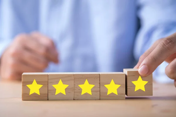 木製の立方体に印刷された黄色の星を置くビジネスマンの手 お客様評価調査と満足コンセプト — ストック写真