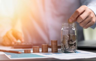 İş adamı tasarruf kavanozuna para koyup hesap makinesi kullanıyor. Finansal muhasebe yatırım kavramı için tasarruf.