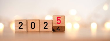 2024 'ten 2025' e ahşap blok küpte yeni yıl hazırlığı için sarı ışık bokeh ve yeni iş hedefi stratejisi kavramına başlamak.