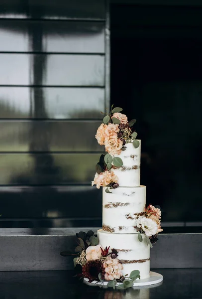 white tiered wedding cake decorated with eucalyptus leaves, powdery-pink roses and carnations