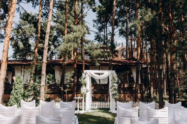 Açık hava düğün töreni. Çiçeklerle süslenmiş beyaz düğün kemeri. düğün kemeri ve kozalaklı ormanda beyaz sandalyeler.