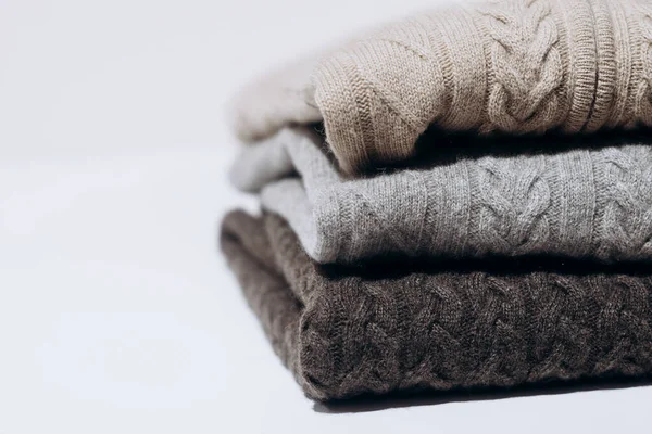 Three folded cashmere knitted sweaters in different shades of gray on white background. three shades of gray. Stack of three sweaters isolated on black background. Knitted wool sweaters.