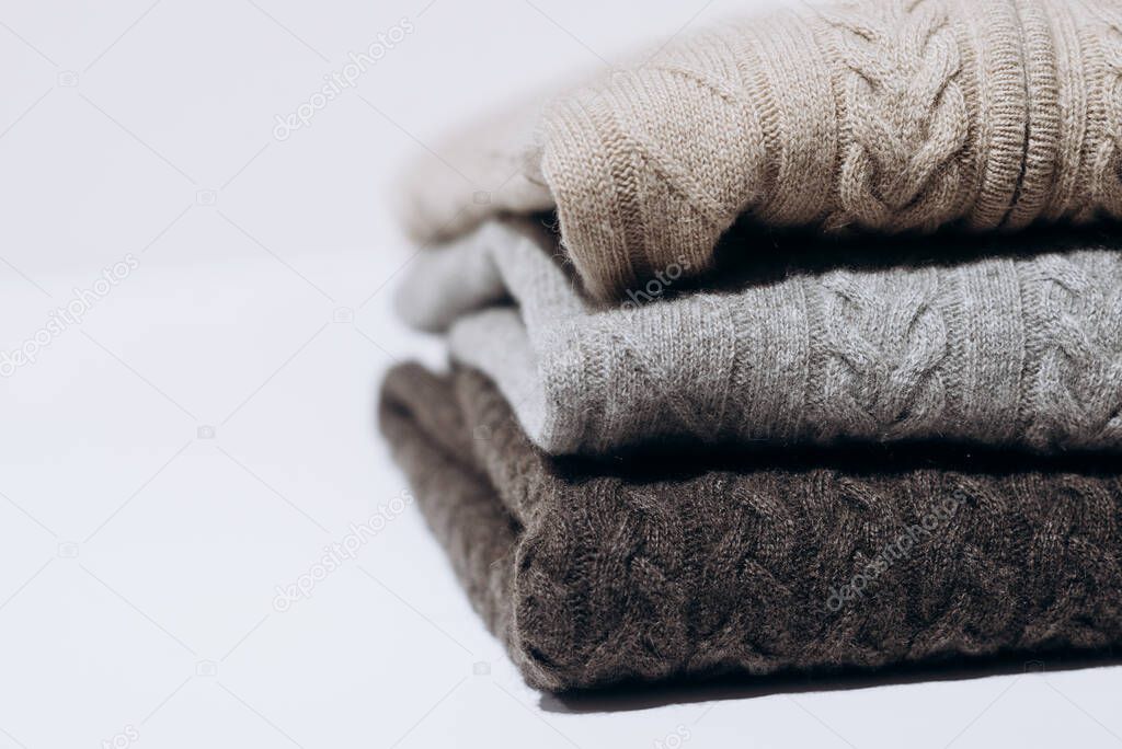 Three folded cashmere knitted sweaters in different shades of gray on white background. three shades of gray. Stack of three sweaters isolated on black background. Knitted wool sweaters.