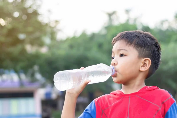 Portrait image of child 5-6 years old. Happy Asian child student boy drinking some water by a plastic bottle. After finished from exercise. Healthy kid and food. Summer season. On green background.