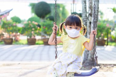 Mutlu Asyalı kız çocuğu gülümsüyor ve kumaş maske takıyor. Çocuk parkında, sosyal mesafede sürgülü bar oyuncağıyla oynuyor. Çocuk konseptini öğrenmek ve aktif olmak.