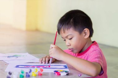 5 yaşındaki bir çocuğun portresi. Asyalı öğrenci odadaki kağıda renkler çiziyor ve boyuyor. Evden öğrenim, sosyal uzaklık, çocuk ve eğitim kavramı.