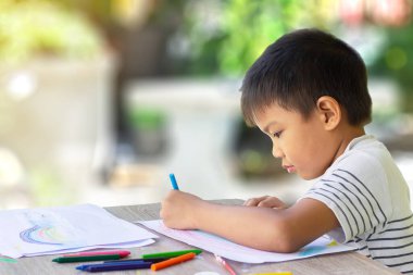 5 yaşındaki bir çocuğun portresi. Asyalı öğrenci odadaki kağıda renkler çiziyor ve boyuyor. Evden öğrenim, sosyal uzaklık, çocuk ve eğitim kavramı.