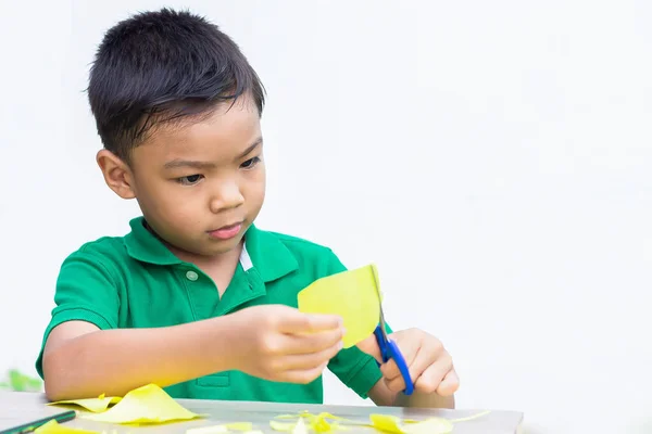 Portrait image of 5-6 years old Asian child boy practice to cutting color paper by the scissors on the wooden table.Study from home, social Distancing, Kid and education concept.