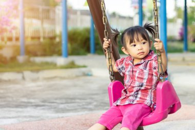 2 yaşındaki bir bebeğin portresi. Neşeli Asyalı kız çocuğu gülümsüyor ve çocuk parkında salıncak koltuğu oyuncağıyla oynarken. Çocuklar ve gelişim konsepti.