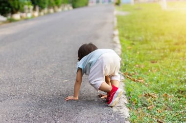 Asyalı kız bebek çim tarlasında yürüme alıştırması yapıyor. Düşüyor ve yerde oturuyor. Bir yaşındaki bir bebeğin gelişimi. Çocuk sağlığı için egzersiz..