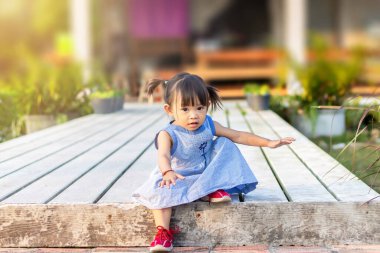 Bebek konseptinin gelişimi, 2 yaşındaki Asyalı bebek kız çocuğunun bahçe parkında merdivenle yürümesi ve ayakta durması. Mavi bir elbise giyiyor..