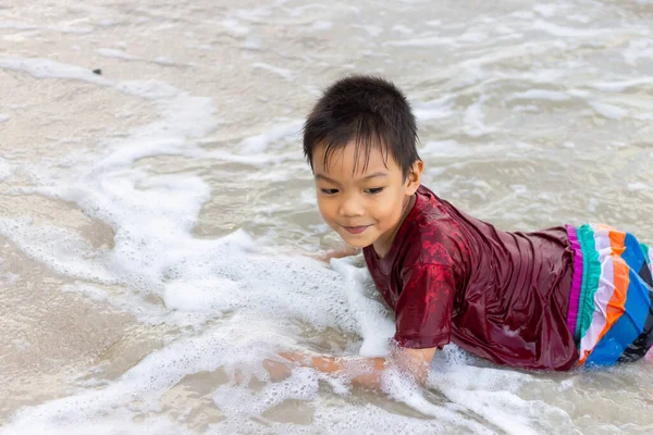 5 yaşındaki bir bebeğin portresi. Mutlu Asyalı çocuk gülümsüyor ve sahilde kumlarla oynuyor. Yaz sezonu. Çocuk ve seyahat konsepti.