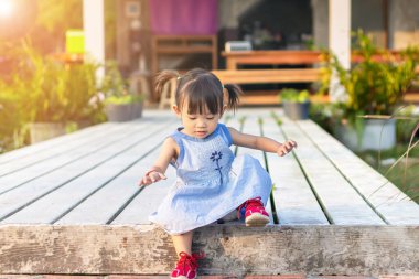 Bebek konseptinin gelişimi, 2 yaşındaki Asyalı bebek kız çocuğunun bahçe parkında merdivenle yürümesi ve ayakta durması. Mavi bir elbise giyiyor..