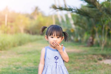 2 yaşındaki bir bebeğin portresi. Asyalı kız ellerini ağzına soktu ve oyun alanında parmaklarını ısırdı. Kişisel hijyen ve çocuk sağlığı konsepti.