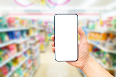 Arka planda bulanık bir süpermarkette boş bir akıllı telefon ekranını tutan bir elin görüntüsünü oluşturun. İnternetten alışveriş kavramı.