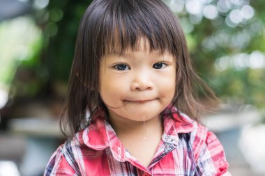 2-3 yaşlarındaki bir bebeğin portresi. Gülümseyen ve kameraman görünümlü mutlu Asyalı kız çocuğu. Yeşil bahçe bahçesinde. Dinlenme zamanı..