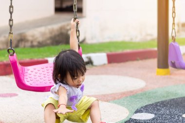 Yumuşak odaklanma. Çocuklar ve güvensiz durum konsepti, çocuk parkında, Asyalı kız bebek sallanan koltuktan düşüyor..