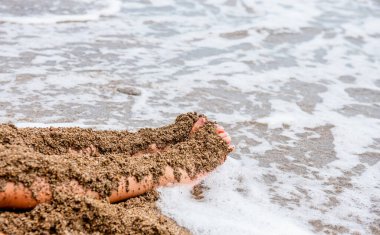 Çocuk kumsalda oynuyor. Bebek elleri ve ayakları kumsalda, yakın planda. Bir çocuk kumdan kale inşa ediyor. Deniz kıyısında bir çocuk. Okyanus kıyısında. Deniz kenarındaki kirli kumlar