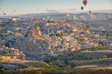 Arka planda Ortahisar ile güneş doğarken Cappadocia 'nın üzerinde uçan balonlarla çekilmiş manzara.