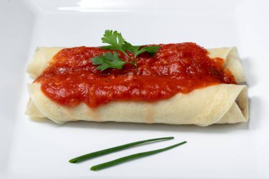 Lezzetli kırmızı domates soslu gözleme. Mavi arka planda beyaz bir tabakta servis ediliyor.