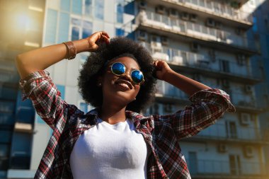 Pozitif duygular ve insanlar, kıvırcık siyah saçlı, mutlu siyahi Amerikalı kadın kavramını benimsiyor. Şehir arka planında. 