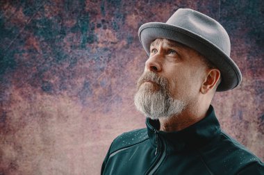 Gri sakallı yaşlı adam fötr şapka takıyor.