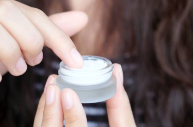 Güzel bir kadının elleri, yüzüne serum kolajen nemlendirici dökerek berrak sarı şişe yumuşak ışık arka planına döküyor. Koruyucu cilt bakımı yüz özü yağı, C vitamini güzellik ve kaplıca.